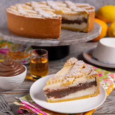 Fetta di crostata con ricotta e crema al cioccolato spolverata di zucchero a velo servita su piatto
