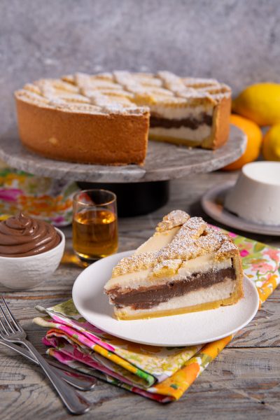 Fetta di crostata con ricotta e crema al cioccolato spolverata di zucchero a velo servita su piatto