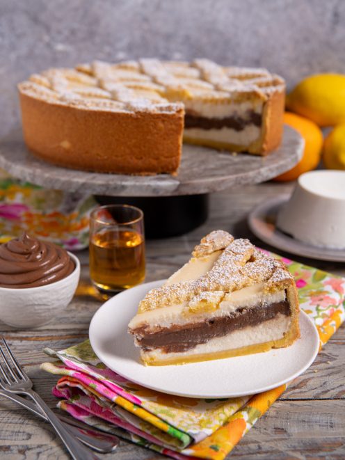 Fetta di crostata con ricotta e crema al cioccolato spolverata di zucchero a velo servita su piatto