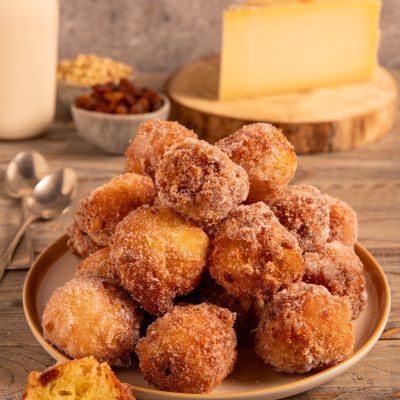 Frittelle al Montasio impilate su un piatto, dorate e croccanti nello zucchero, con una tagliata a meta