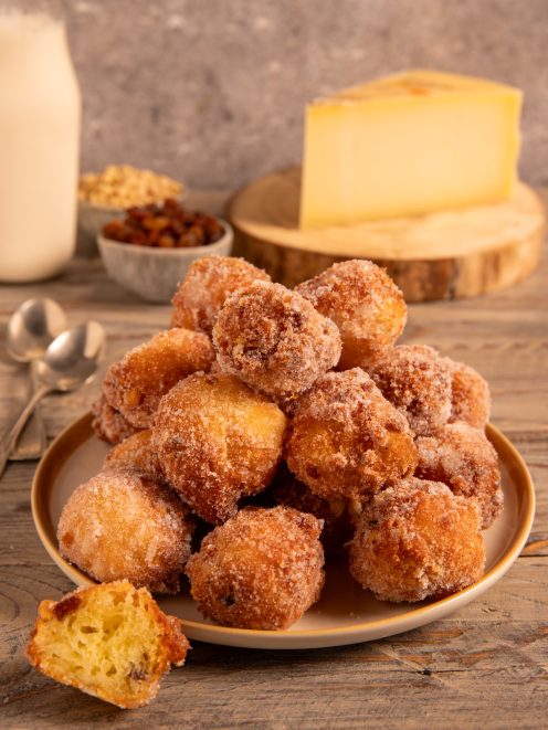 Frittelle al Montasio impilate su un piatto, dorate e croccanti nello zucchero, con una tagliata a meta
