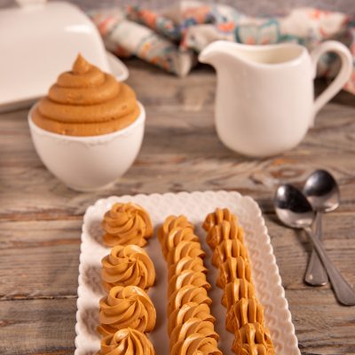 Ganache al caramello salato disposta in ciuffi e strisce decorative su vassoio traforato