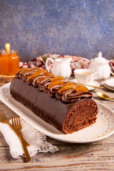 Tronchetto Sacher glassato al cioccolato con ciuffi di crema e scorze di arancia candita