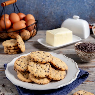 Biscotti con gocce di cioccolato dorati e friabili, serviti in abbondanza con burro e uova sullo sfondo