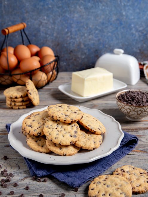 Biscotti con gocce di cioccolato dorati e friabili, serviti in abbondanza con burro e uova sullo sfondo