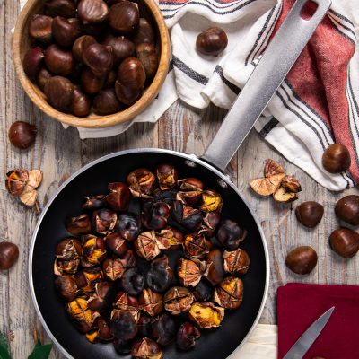 Castagne in padella arrostite con la buccia incisa, accanto a castagne crude
