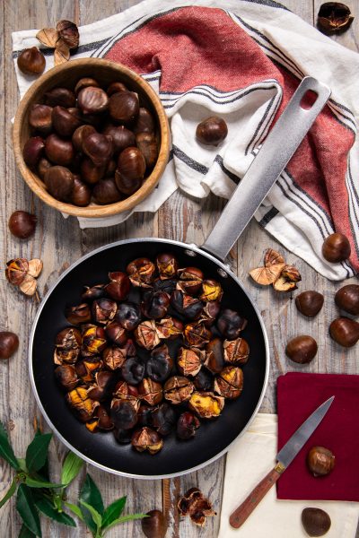 Castagne in padella arrostite con la buccia incisa, accanto a castagne crude