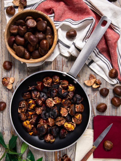 Castagne in padella arrostite con la buccia incisa, accanto a castagne crude