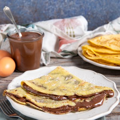Crepes alla Nutella piegate a triangolo con crema al cioccolato che cola e zucchero a velo