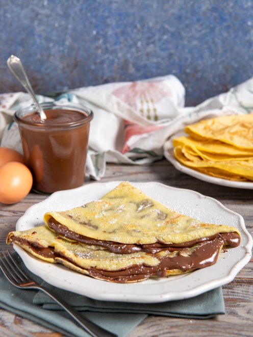 Crepes alla Nutella piegate a triangolo con crema al cioccolato che cola e zucchero a velo