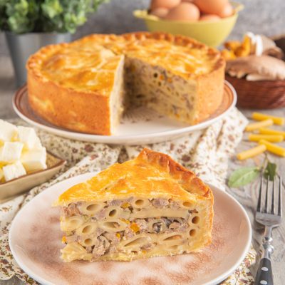 Pasticcio di maccheroni alla ferrarese con crosta dorata, farcito di ragù e funghi in una fetta appena tagliata