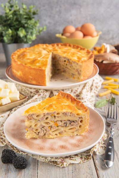 Pasticcio di maccheroni alla ferrarese con crosta dorata, farcito di ragù e funghi in una fetta appena tagliata