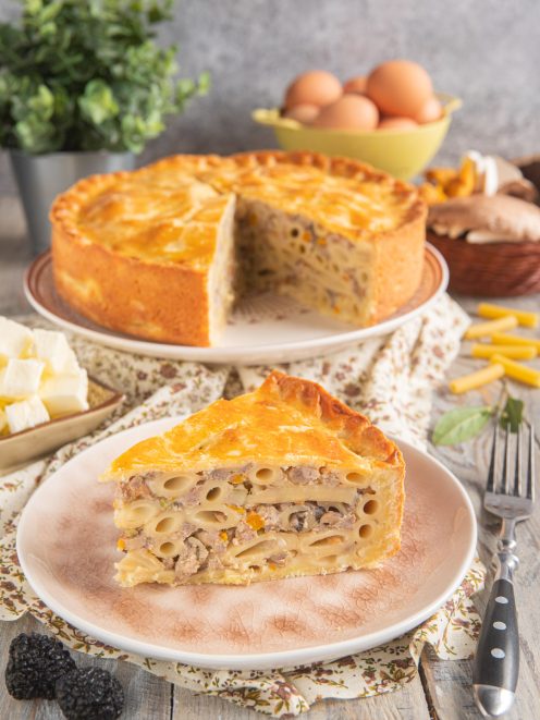 Pasticcio di maccheroni alla ferrarese con crosta dorata, farcito di ragù e funghi in una fetta appena tagliata