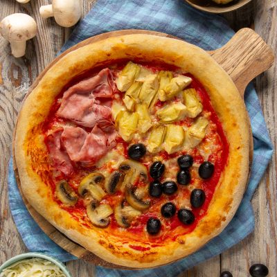 Pizza quattro stagioni con prosciutto cotto, carciofi, funghi e olive nere su salsa di pomodoro