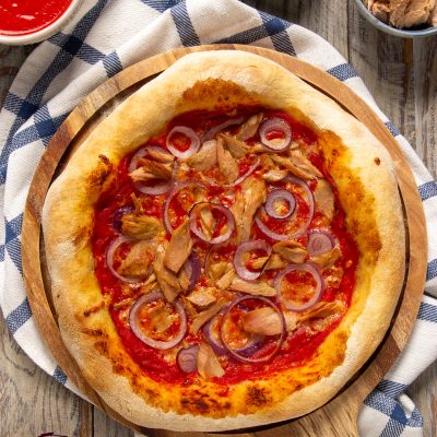 Pizza con tonno e cipolle rosse su salsa di pomodoro, con bordo dorato e croccante