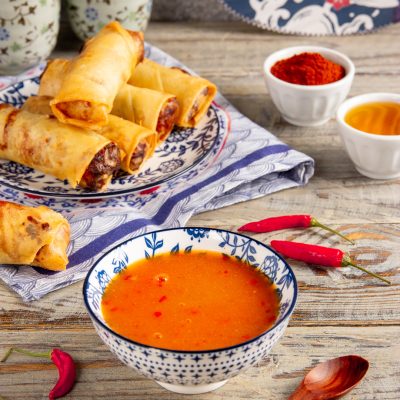 Salsa agrodolce piccante in ciotola, con involtini primavera fritti e peperoncini freschi