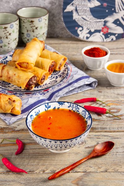 Salsa agrodolce piccante in ciotola, con involtini primavera fritti e peperoncini freschi