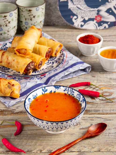 Salsa agrodolce piccante in ciotola, con involtini primavera fritti e peperoncini freschi