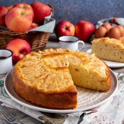 Torta di mele cremosa con fette di mela in superficie, una fetta già tagliata che mostra l'interno soffice