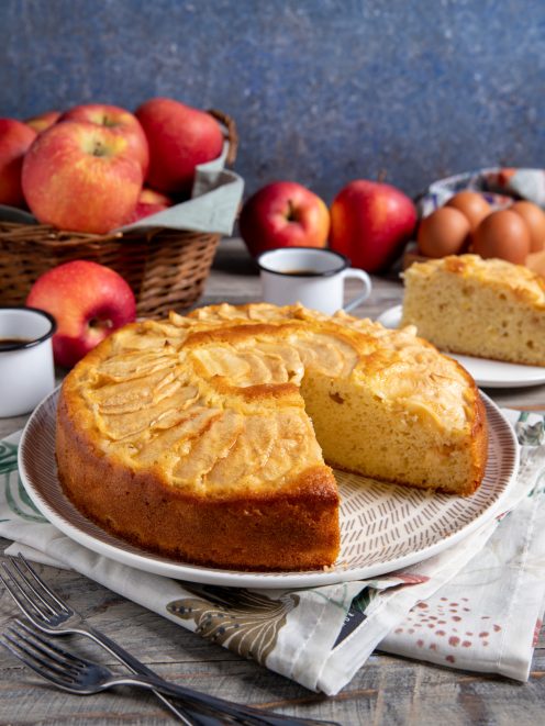 Torta di mele cremosa con fette di mela in superficie, una fetta già tagliata che mostra l'interno soffice