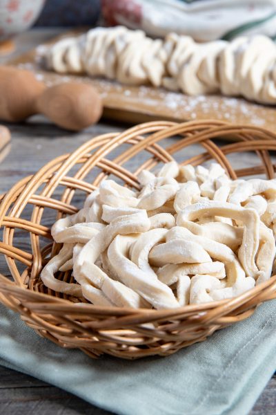 Udon freschi appena tagliati raccolti in un cestino, con altri sfilacci di pasta sullo sfondo