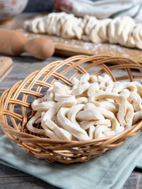 Udon freschi appena tagliati raccolti in un cestino, con altri sfilacci di pasta sullo sfondo