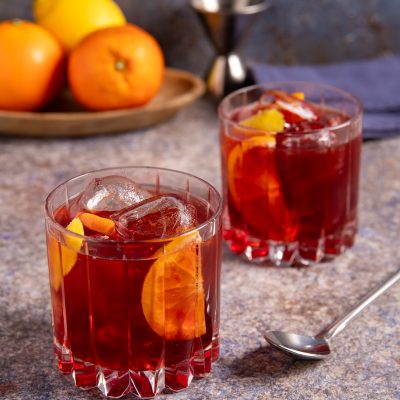 Americano cocktail servito in due bicchieri bassi con fetta di arancia, scorza di limone e cubetti di ghiaccio