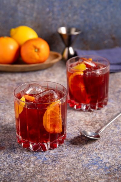 Americano cocktail servito in due bicchieri bassi con fetta di arancia, scorza di limone e cubetti di ghiaccio