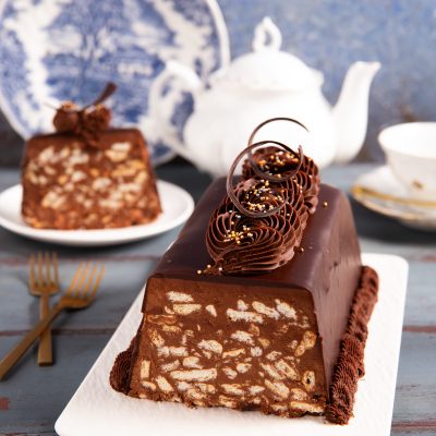 Chocolate biscuits cake in fetta, con interno a pezzi di biscotto e glassa lucida decorata con riccioli di cioccolato e perline dorate