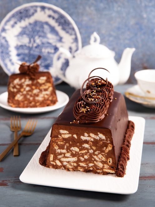 Chocolate biscuits cake in fetta, con interno a pezzi di biscotto e glassa lucida decorata con riccioli di cioccolato e perline dorate