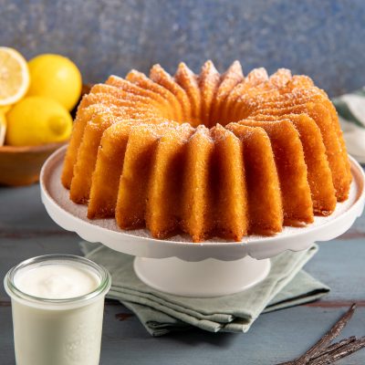Ciambella allo yogurt con superficie dorata e scanalata, servita con crema alla vaniglia e limoni