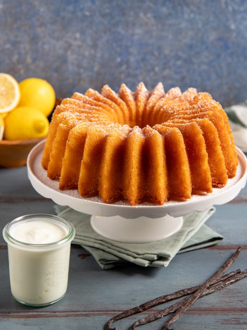 Ciambella allo yogurt con superficie dorata e scanalata, servita con crema alla vaniglia e limoni