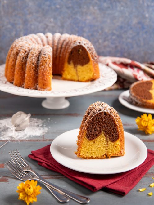 Ciambella bicolore con impasto vaniglia e cacao, spolverata di zucchero a velo, servita a fette