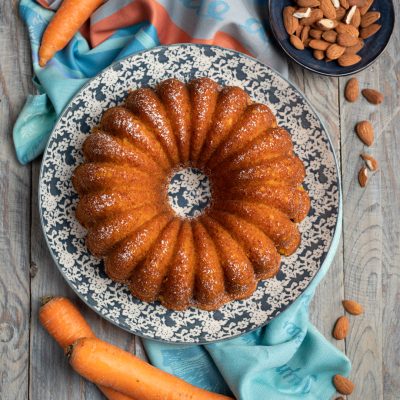 Ciambella di carote e mandorle spolverata di zucchero a velo, con carote fresche intorno