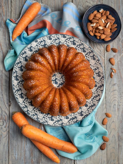 Ciambella di carote e mandorle spolverata di zucchero a velo, con carote fresche intorno