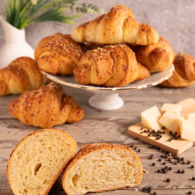 Croissant sfogliati cacio e pepe tagliati a metà, con la mollica alveolata in primo piano e grani di pepe nero accanto