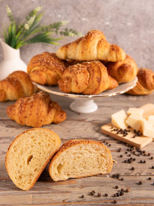 Croissant sfogliati cacio e pepe tagliati a metà, con la mollica alveolata in primo piano e grani di pepe nero accanto