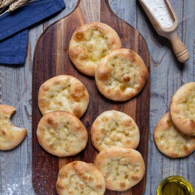 Focaccine genovesi dorate con olio d'oliva lucido in superficie, disposte su un tagliere