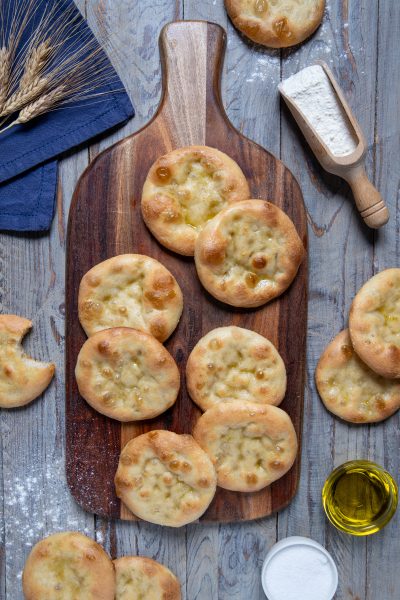 Focaccine genovesi dorate con olio d'oliva lucido in superficie, disposte su un tagliere