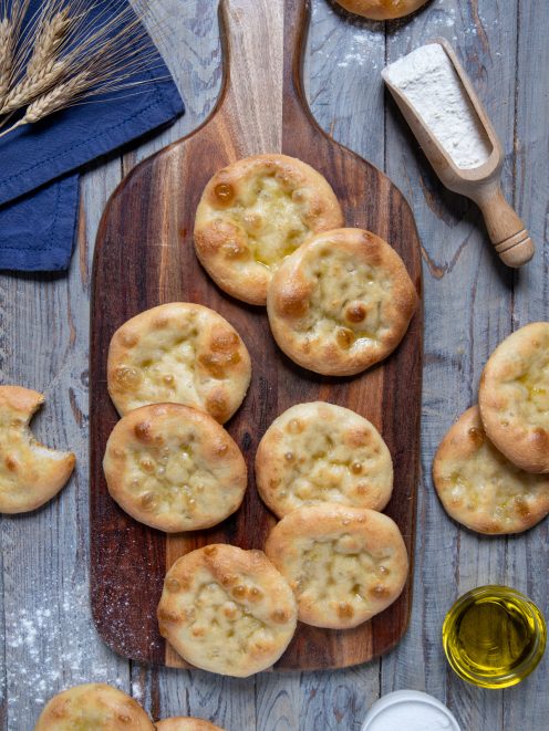 Focaccine genovesi dorate con olio d'oliva lucido in superficie, disposte su un tagliere