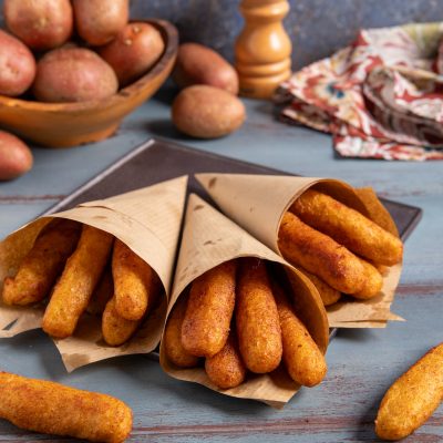 Panzarotti napoletani fritti serviti in tre cartocci di carta, con patate rosse sullo sfondo