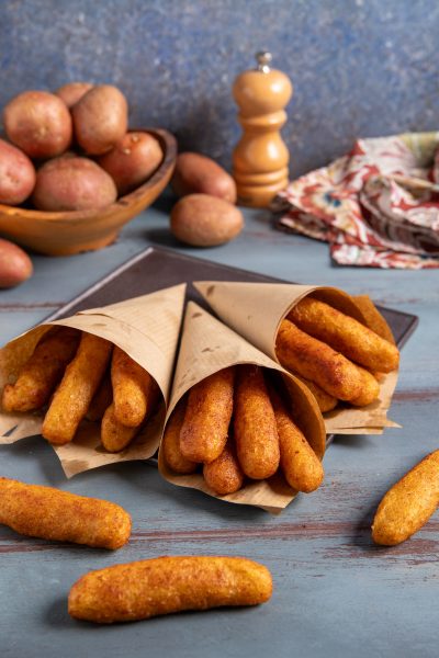 Panzarotti napoletani fritti serviti in tre cartocci di carta, con patate rosse sullo sfondo