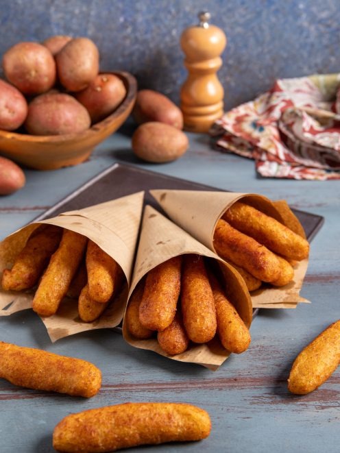 Panzarotti napoletani fritti serviti in tre cartocci di carta, con patate rosse sullo sfondo