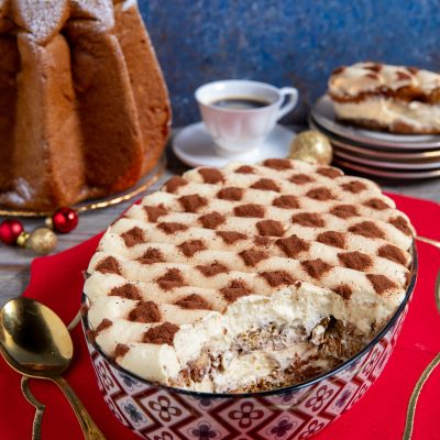 Tiramisù con pandoro in ciotola decorata, crema al mascarpone e cacao a scacchi, con una porzione già servita