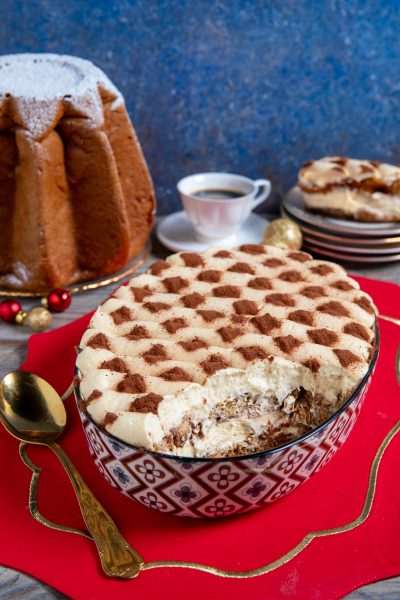 Tiramisù con pandoro in ciotola decorata, crema al mascarpone e cacao a scacchi, con una porzione già servita