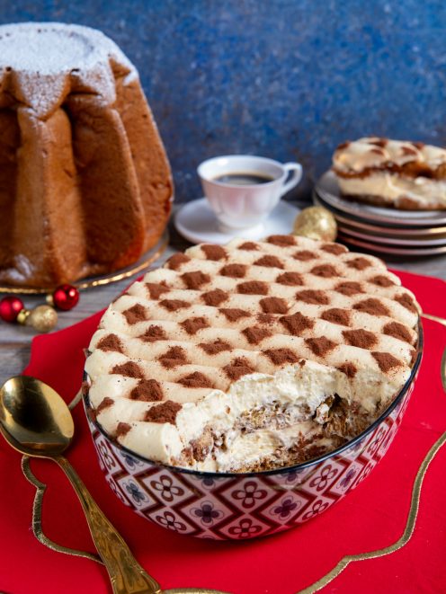 Tiramisù con pandoro in ciotola decorata, crema al mascarpone e cacao a scacchi, con una porzione già servita