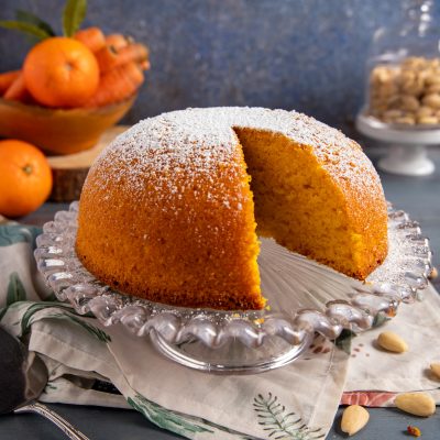 Torta Camilla con una fetta tagliata che rivela la mollica arancione, spolverata di zucchero a velo