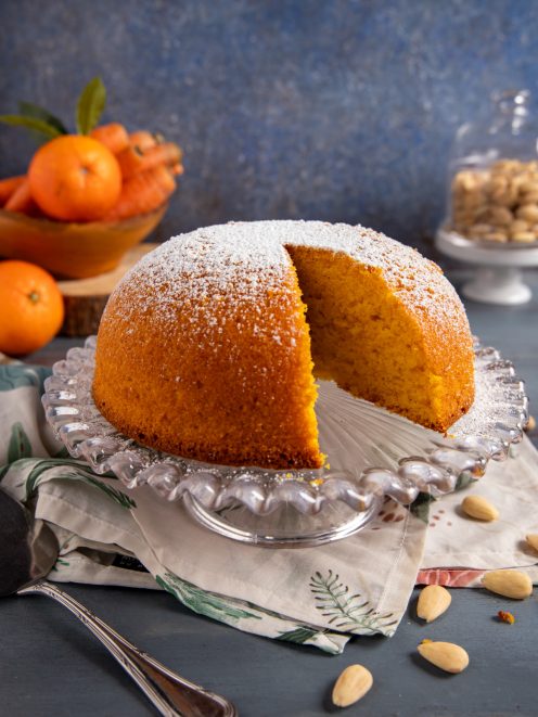 Torta Camilla con una fetta tagliata che rivela la mollica arancione, spolverata di zucchero a velo