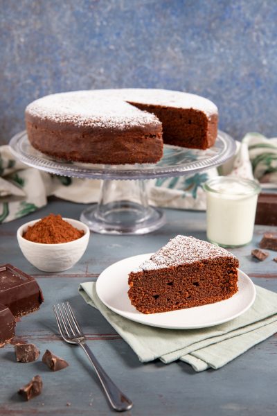 Torta allo yogurt e cioccolato spolverata di zucchero a velo, con una fetta servita sul piatto