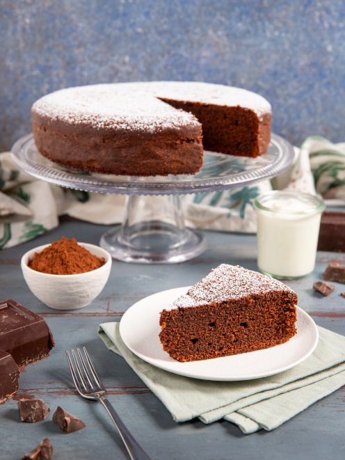 Torta allo yogurt e cioccolato spolverata di zucchero a velo, con una fetta servita sul piatto